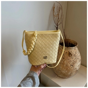 Detail of hand-held woven bucket bag in pale yellow leather with metal logo and strap