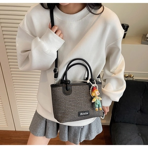 Close-up of woven bucket bag with leather handle and cute doll charm on model