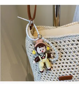 Detail of cute cartoon girl charm with faux pearl strap on a beige woven tote bag