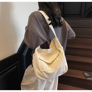Detail of a large cream canvas crossbody bag with a front flap pocket on wooden stairs