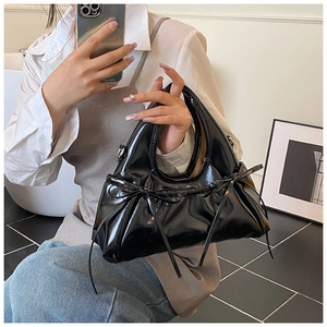 Detail shot of glossy black patent leather crossbody bag with decorative bows