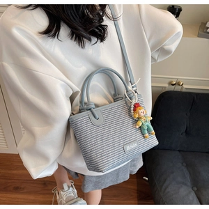 Detail of light blue woven bucket bag with metal logo and cute cartoon charm