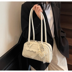 Detail of cream-colored pillow bag with wavy pocket edges and pearl heart charm