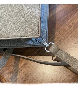 Detailed macro view of silver metal hardware and textured lychee grain leather on taupe bag