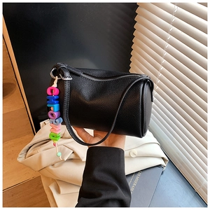 Close-up of black litchi pattern leather cylinder bag with colorful letter charm
