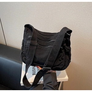 Detail of black canvas crossbody bag showing multiple zipper pockets and adjustable strap