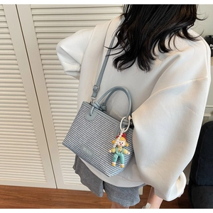 Blue woven bucket bag with pearl doll charm shown on model against white shutters