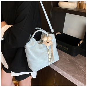 Detail of light blue faux crocodile bucket bag with plush bear charm and adjustable strap