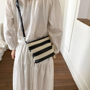 Detail of a black and white striped woven crossbody bag with thin leather strap