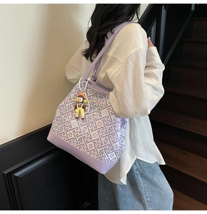 Purple tote bag with geometric patterns and cartoon charm shown on model's shoulder