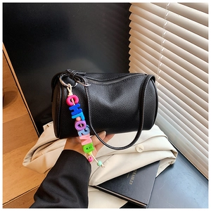 Detailed close-up of a black lychee-grain cylinder bag with a stylish colorful letter charm