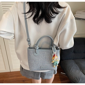 Light blue woven bucket bag with leather strap and cute character charm on a white top