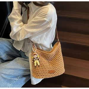 Close-up of a woven straw shoulder bag with leather straps and a cute cartoon doll pendant