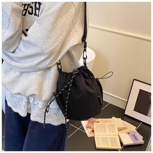 Detail of a black nylon drawstring bucket bag with decorative woven cord and strap