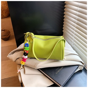 Close-up of lime green litchi grain cylinder bag with colorful letter charms and long strap