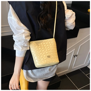 Detail of pale yellow bucket bag with woven texture and gold logo on casual outfit