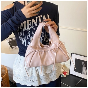 Detail of pink patent leather handbag with bow accents and pleated moon bag design