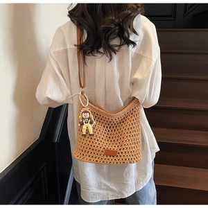 Detail of hand-woven brown straw shoulder bag with a cute cartoon doll charm