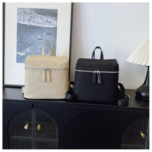 Dual-zipper nylon backpacks in black and beige displayed on a vintage cabinet