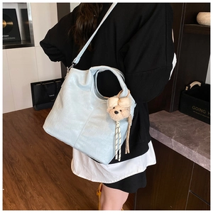 Detail of light blue crocodile embossed tote bag with teddy bear charm on a female model