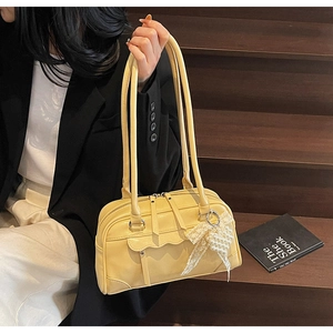 Detail of yellow baguette bag with scalloped edges and pearl bow charm accessory