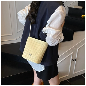 Detail view of yellow woven bucket bag with fine leather texture and metal logo