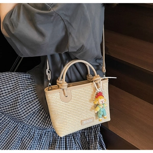 Woven straw bucket bag with circular handles and a cute doll charm worn by a model