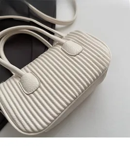 Detail of white women handbag featuring horizontal pleated quilting and dual round handles