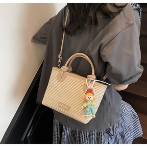 Detail of woven straw bucket bag featuring beige texture and faux leather trim with charm