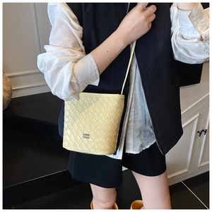 Detail view of the hand-woven leather texture and metal logo on the yellow bucket bag