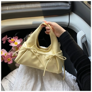 Detailed shot of cream-colored pleated handbag with bow accents and embossed text