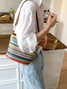 Colorful striped woven bucket bag with brown leather strap worn in a lifestyle setting