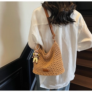 Detail of a brown hand-woven hobo bag with adjustable strap and cute doll charm accessory