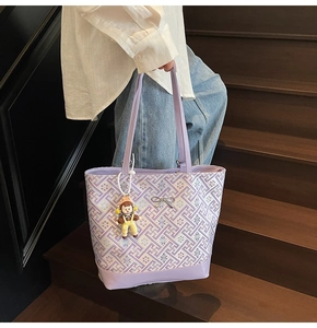 Detail of purple tote bag with geometric patterns, metal bow, and cartoon girl charm