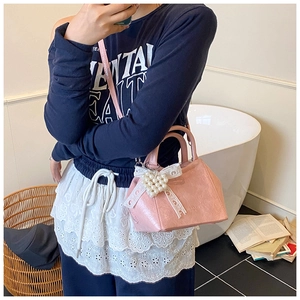 Dettaglio della borsa rosa con ciondolo a cuore di perle e fiocco indossata dalla modella