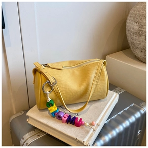 Detail of yellow lychee leather cylinder bag with colorful letter bead charm on a book