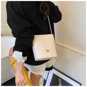 Detail of cream woven bucket bag showing premium cross-weave texture and metal logo plate