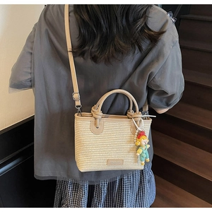 Detailed shot of beige woven bucket bag with pearl doll charm on a casual outfit