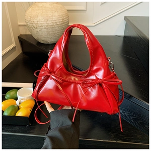 Detail of red pleated handbag featuring bow decorations and shiny synthetic leather