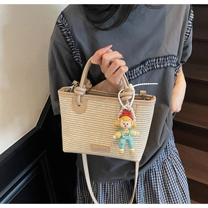Close-up of beige woven straw bucket bag with leather handles and cartoon doll pendant