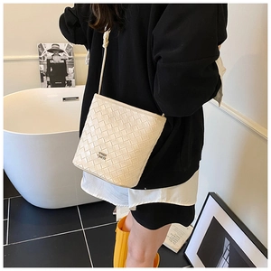 Detail shot of cream woven bucket bag with metal logo and shoulder strap on model