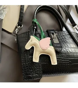 Close-up of a playful horse charm on a black crocodile-patterned leather handbag