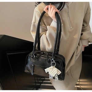 Detail of black glossy shoulder bag featuring layered wavy design and pearl bow charm