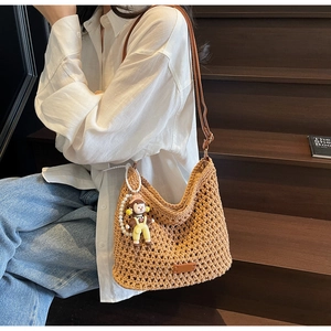 Detail of hand-woven hollow shoulder bag in caramel brown with doll charm on wooden stairs