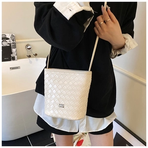 Detail of white woven bucket bag with leather texture and metal logo on a model