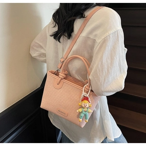 Detail of pink woven bucket bag with cute cartoon charm on a minimalist background