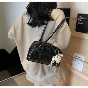 Detail of black faux leather shoulder bag with wavy pocket edge and pearl bow charm