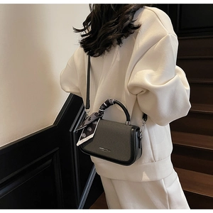 Detail of grey crossbody bag with ribbon-wrapped handle and contrast trim on white outfit