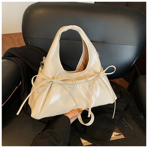 Detail of beige glossy handbag with elegant bow decoration and slender shoulder strap