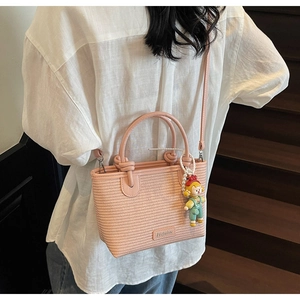 Pink woven bucket bag with long strap and cute clown doll accessory on a female model